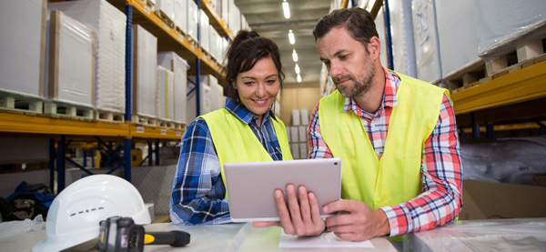 two workers in warehouse looking at a tablet 